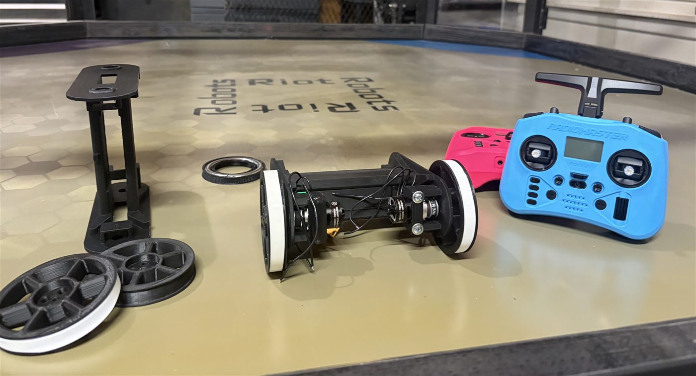 Robot v0.2 drive-base components, spare wheels, frame parts, and controllers arranged inside the arena